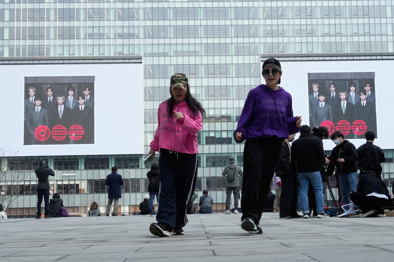 People dance in a square in front of screens showing young men on them.