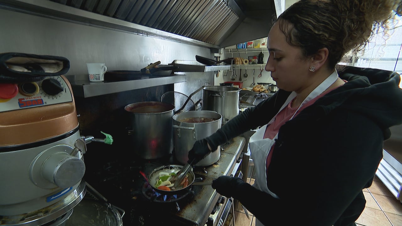Inside a restaurant kitchen, a woman in an apron is preparing food.