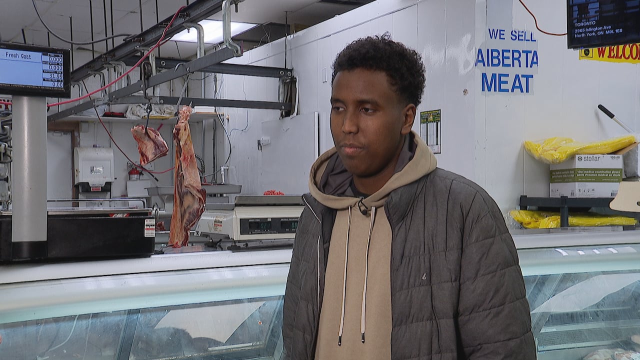 A man wearing a hoodie, standing inside a butcher shop.