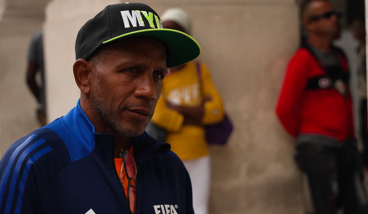 A man wearing a fifa sweater and a cap looks on.