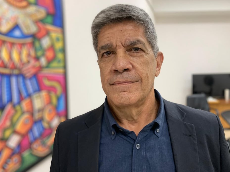 A man standing next to a painting looks on.