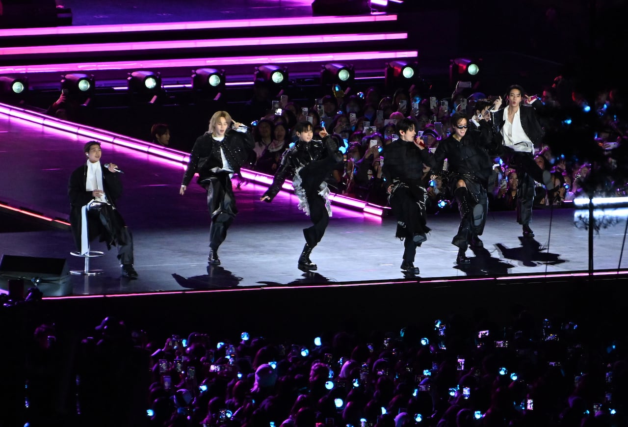 A pop group dances and sings onstage during a concert.