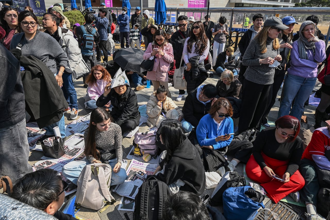 People line up for a concert, with some sitting down.