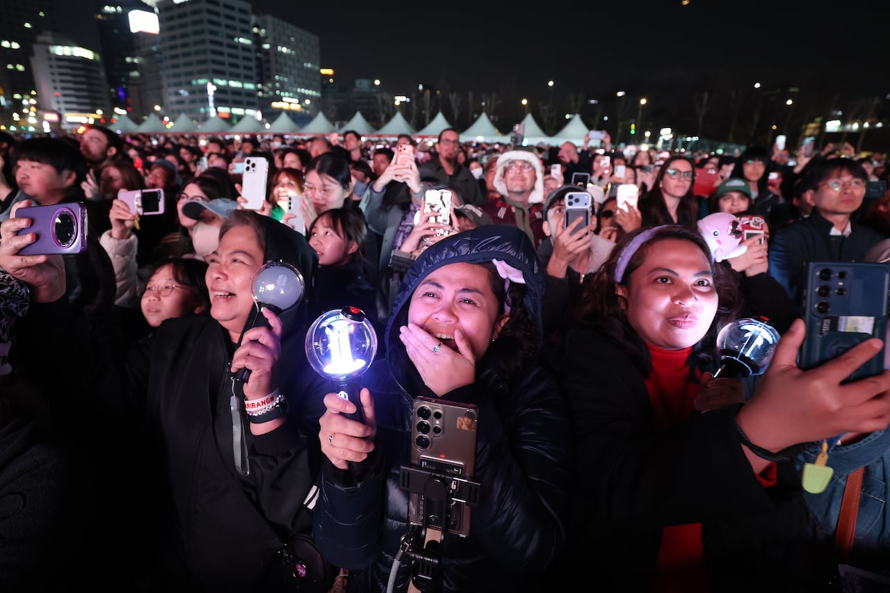 A crowd of people outside holding up phones and smiling while watching a concert. 