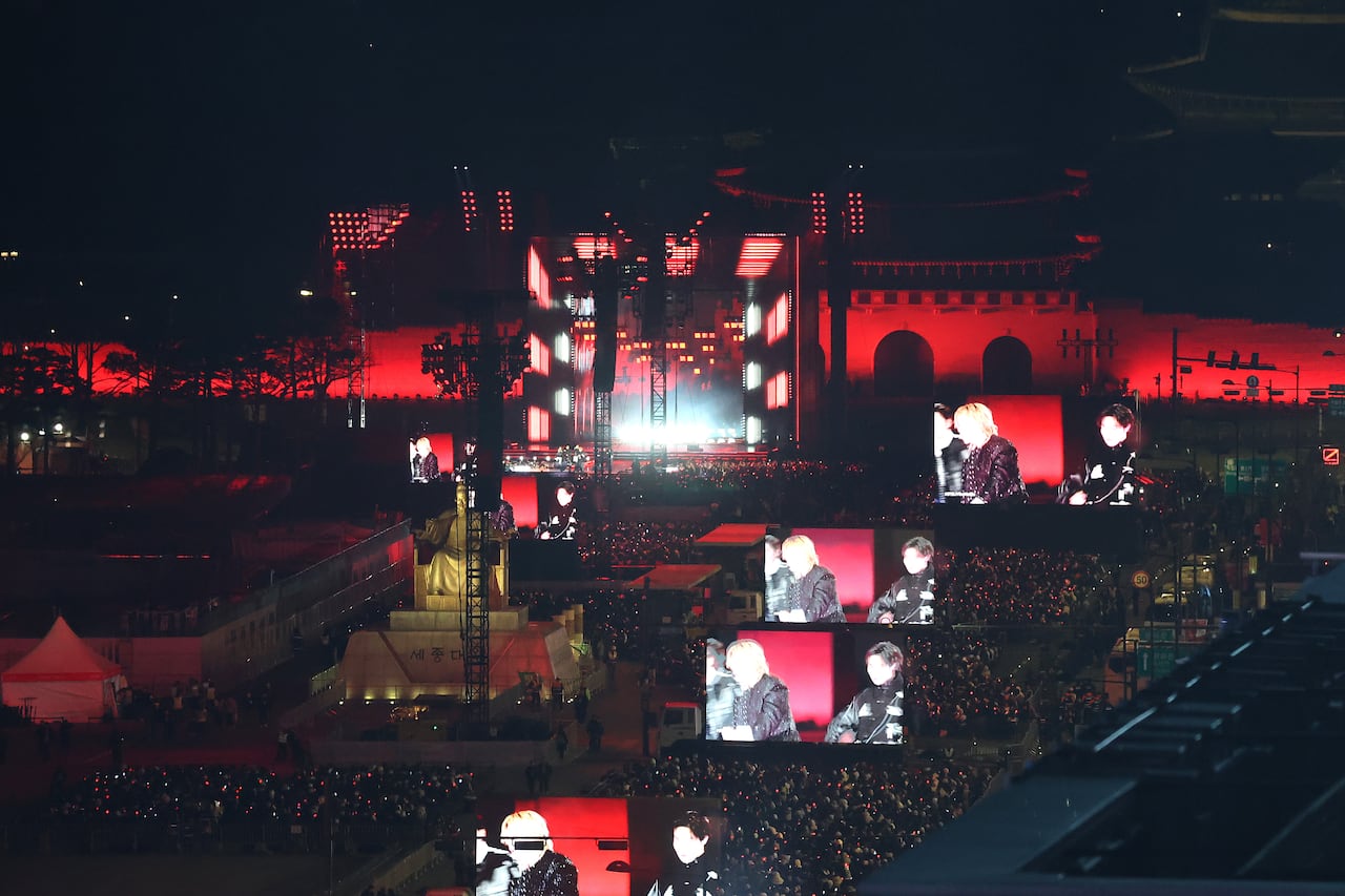 A wide shot of a large crowd at a concert with several large screens. 