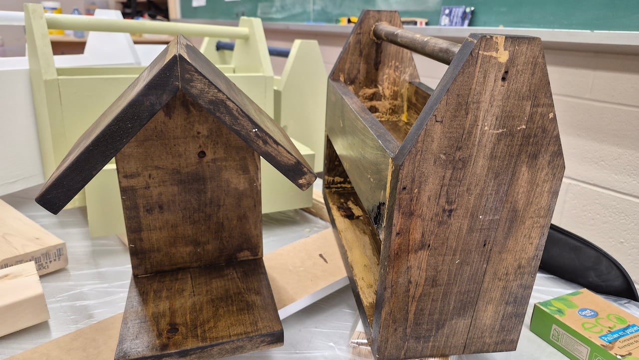 A dark brown birdhouse and a toolbox are seen sitting next to each other. 
