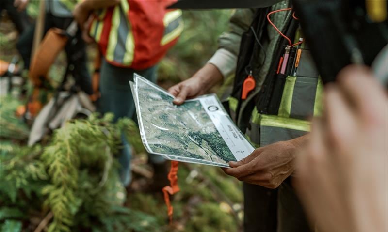 People wearing high-vis vests hold a map in a forest.