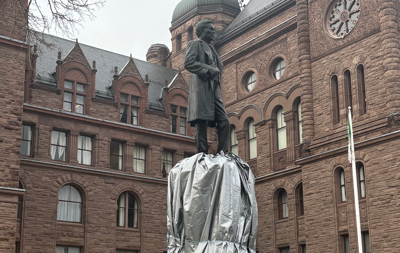 Statue with a fenced barrier around it and wrapped in silver tarp. 