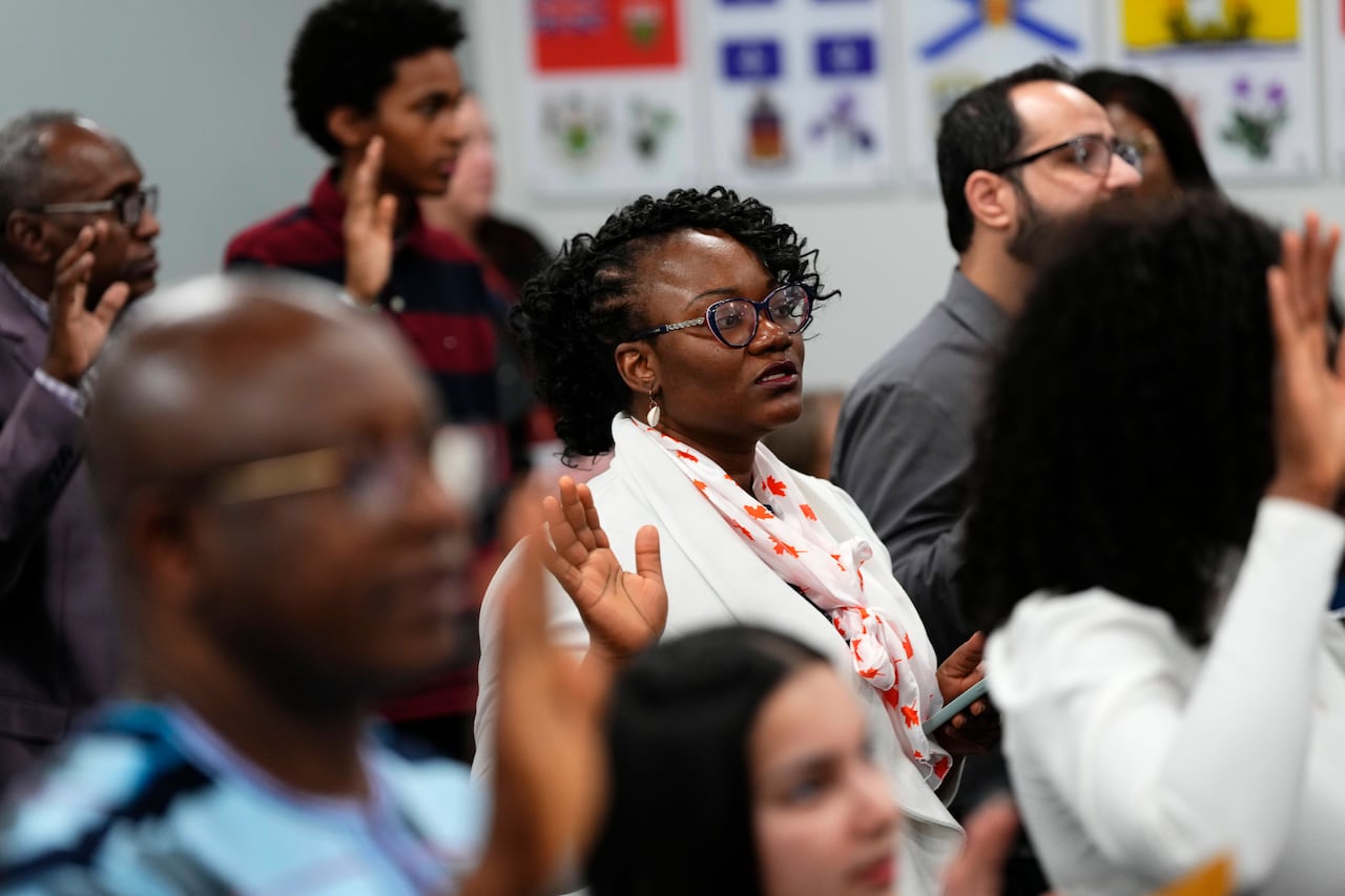 People stand in a crowded room with one hand up as they take their citizenship oath. 