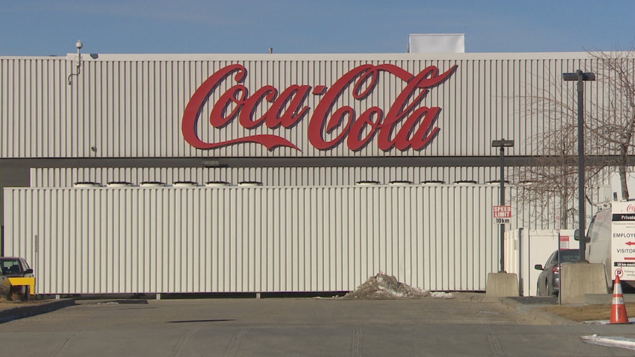 Vehicles are parked outside a factory warehouse with the Coca-Cola logo.