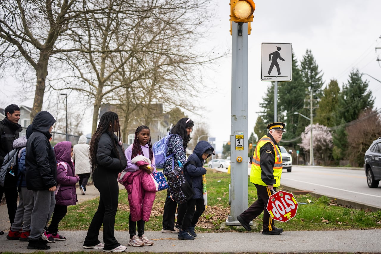 A person in neon watches for cars as a group of children wait behind her