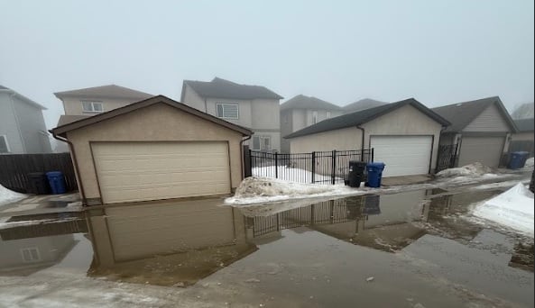 A residential street with garages is seen with water pooling in the road