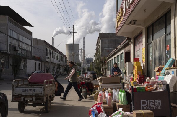 FILE- Guohua Power Station, a coal-fired power plant, operates as people sell items on a street in Dingzhou, Baoding, in northern China's Hebei province, Friday, Nov. 10, 2023. (AP Photo/Ng Han Guan, File)