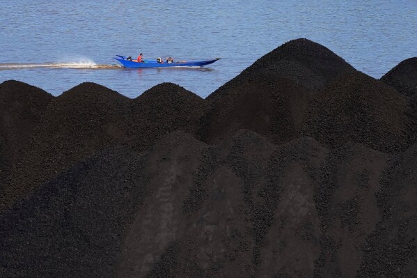 FILE- A boat cruises past a coal barge on Mahakam River in Samarinda, East Kalimantan, Indonesia, on Dec. 19, 2022. (AP Photo/Dita Alangkara, File)