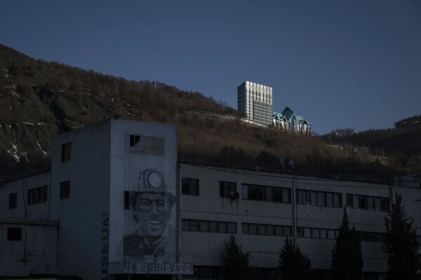FILE- The Gangwon Land Casino sits atop a mountain as a drawing of a coal miner decorates the wall of a building in an abandoned mine in the town of Sabuk, Jeongseon county, South Korea, Saturday, Feb. 17, 2018. The sign below reads ÒI was a miner, an industrial warrior.Ó (AP Photo/Felipe Dana)