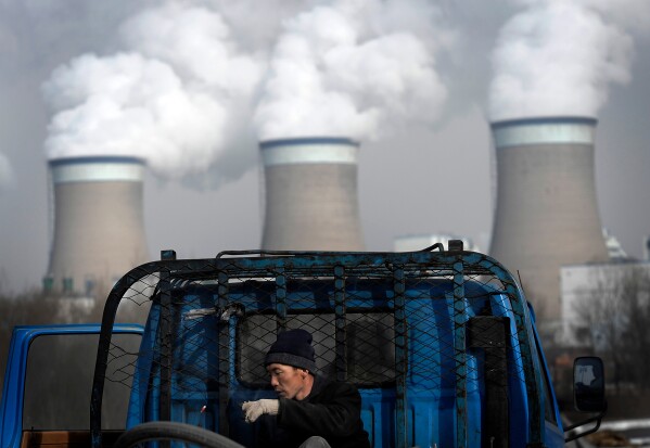 A worker throws his cigarette on a truck parked in front of a cooling towers of a coal-fired power plant in Dadong, Shanxi province, China, on Dec. 3, 2009. (AP Photo/Andy Wong, File)
