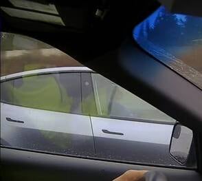 A grainy image appearing to show a Tesla driver with her hands folded.