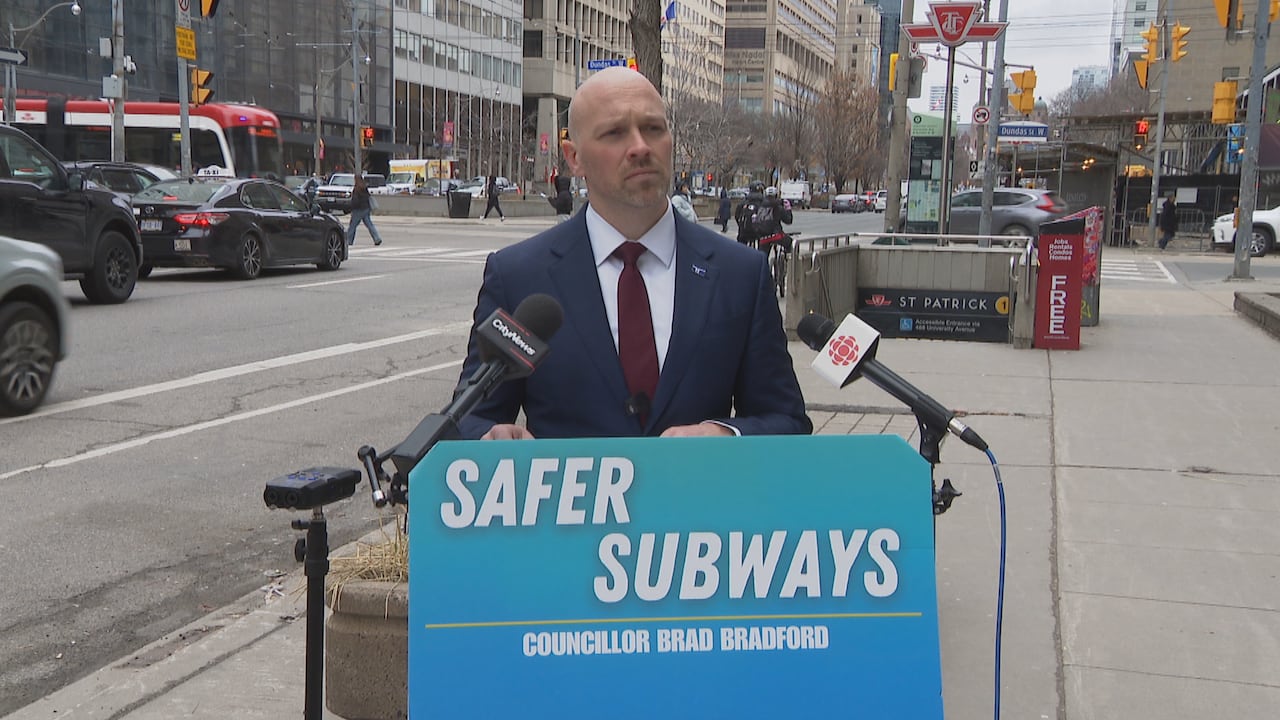 A man stands behind a podium outside a subway station.