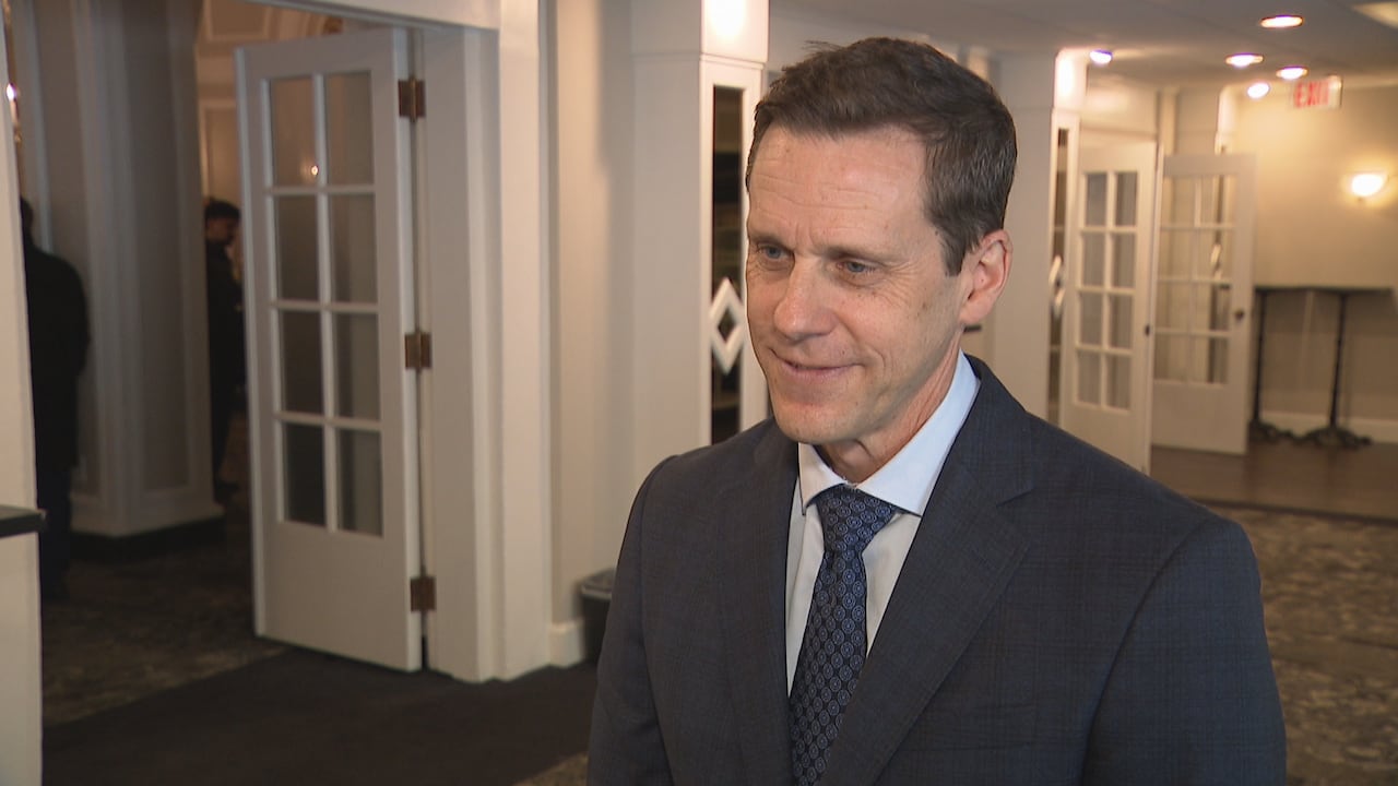A man in a dark suit and blue tie takes questions from a reporter.