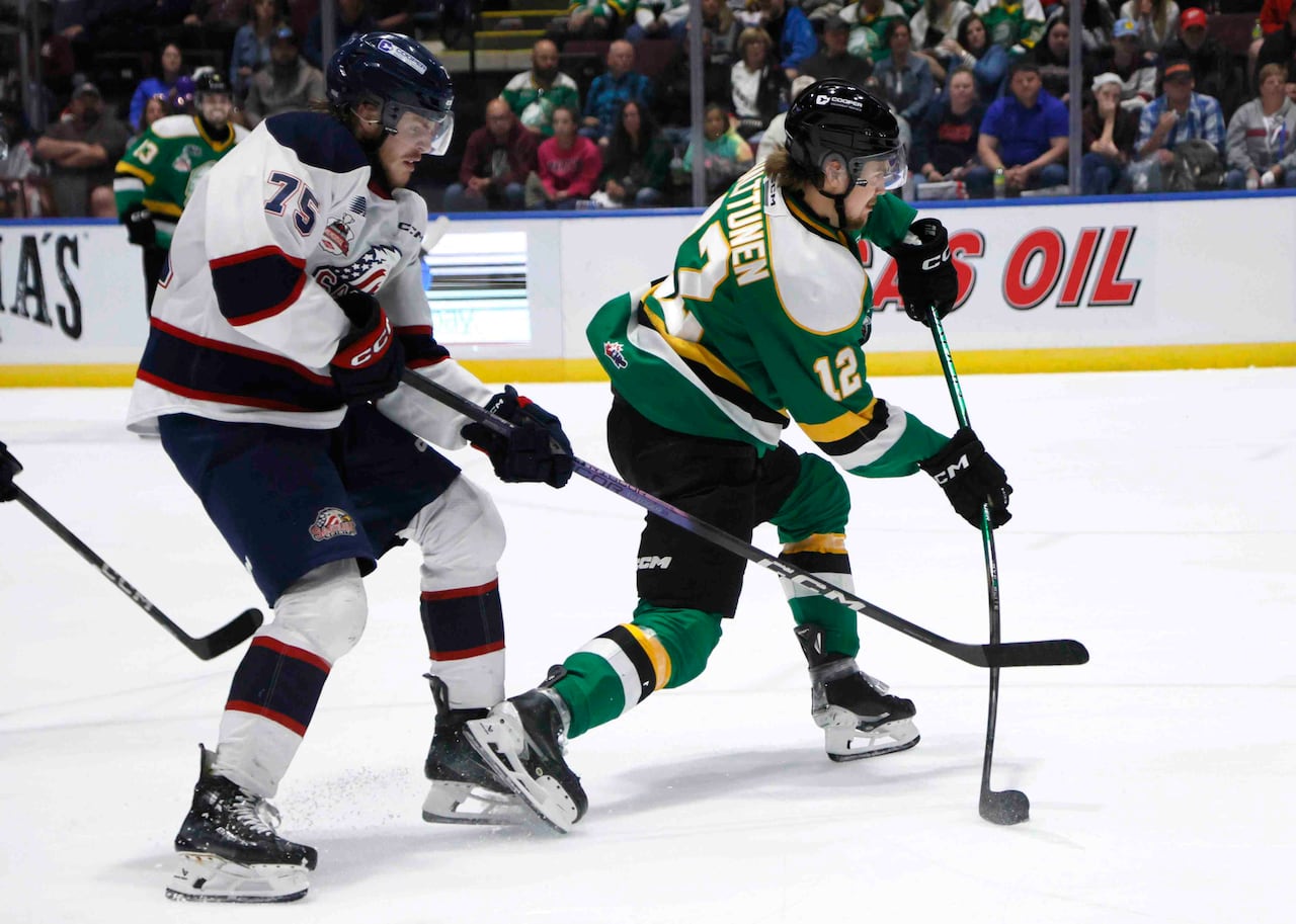 One hockey player chases another who's in the process of taking a shot on goal.