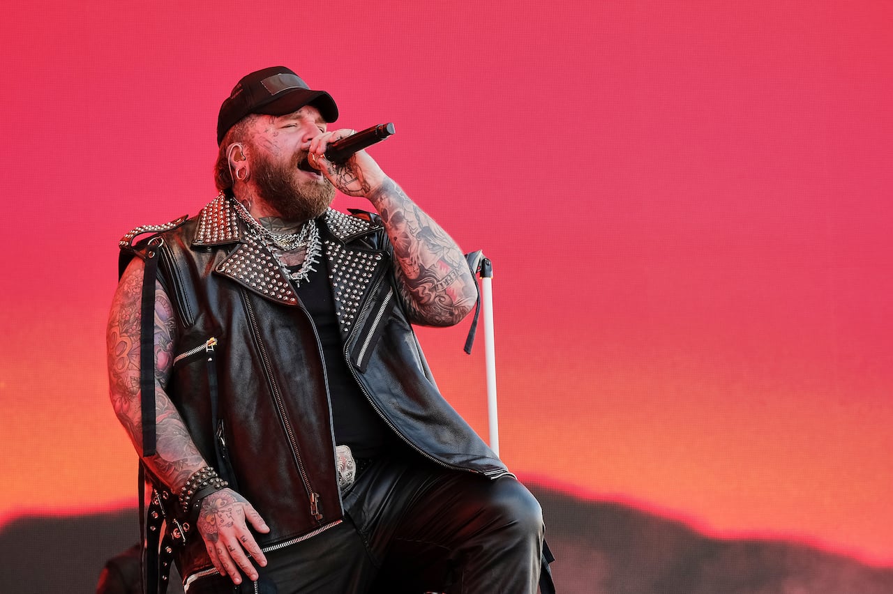 A man with tattooed arms and face sings in front of a pink backdrop.
