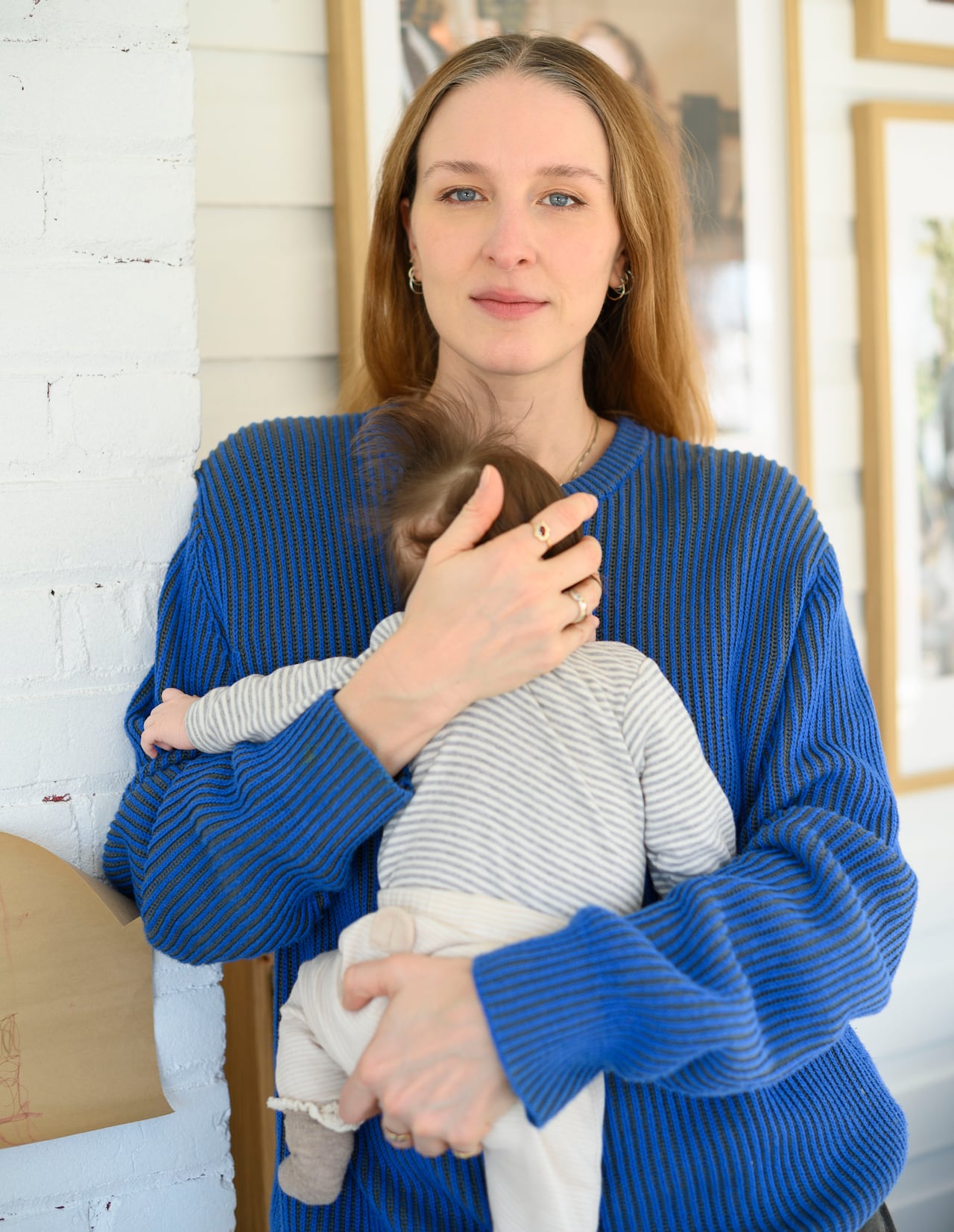A woman with long hair looks at the camera and holds a baby.
