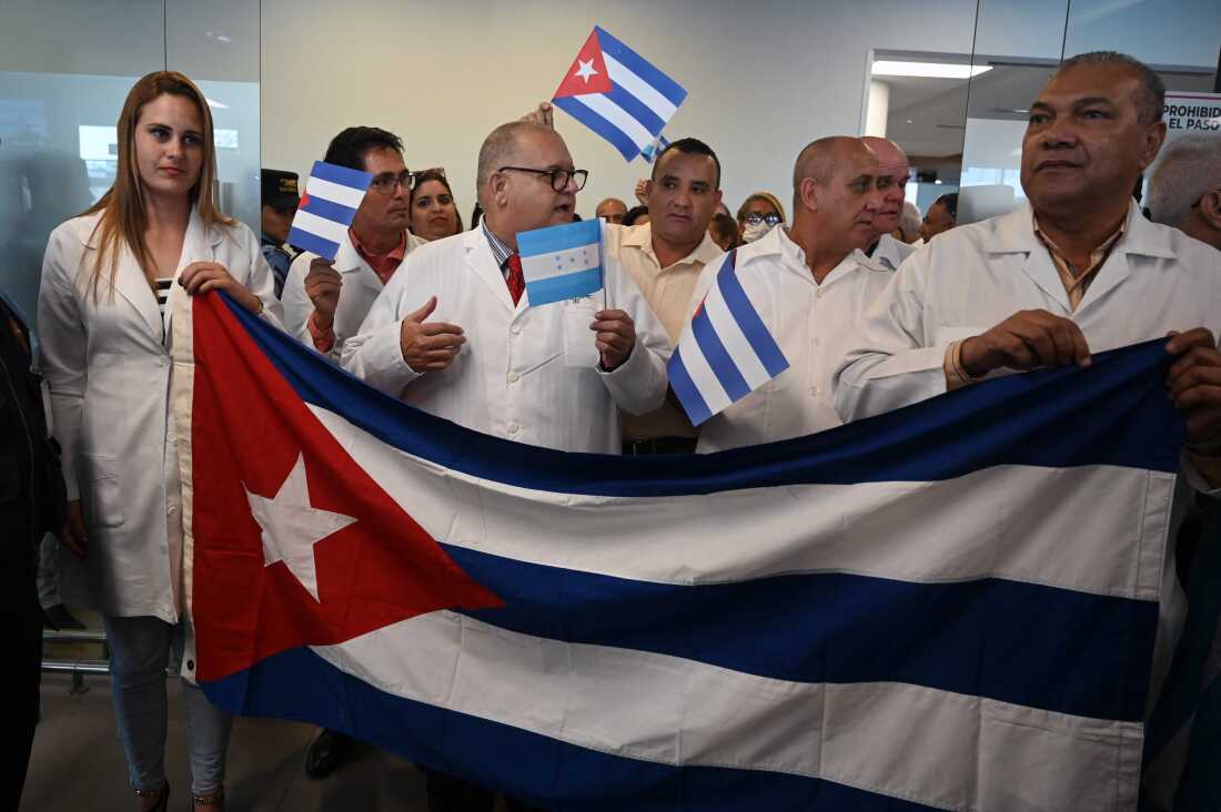 Cuban doctors hold a national flag upon arrival at Palmerola International Airport, 50 kms north of Tegucigalpa, on February 27, 2024. The 100 medical specialists-brigade will stay in Honduras for two years and includes anaesthesiologists, oncologists, neurosurgeons, cardiologists, and endocrinologists. 