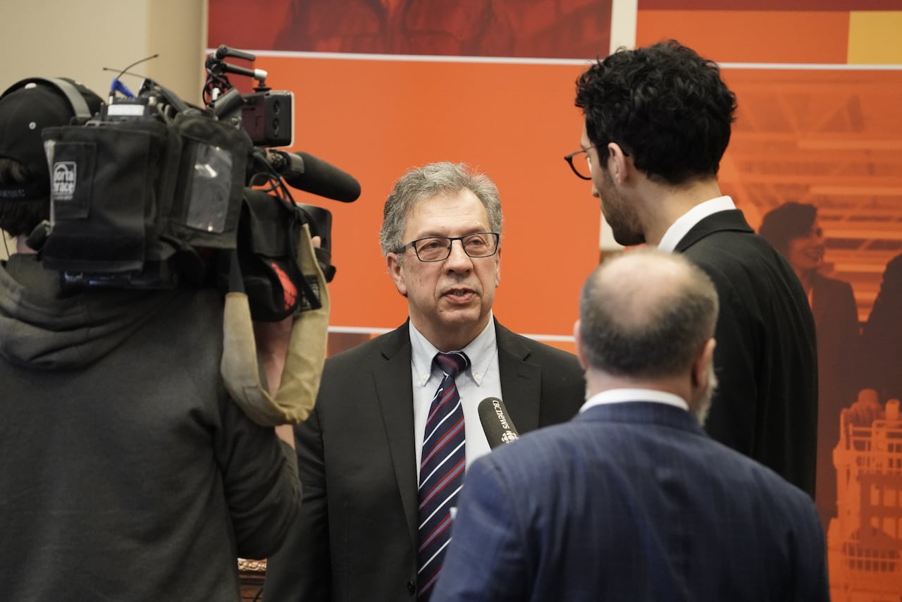 A man in a suit speaks in front of a camera.