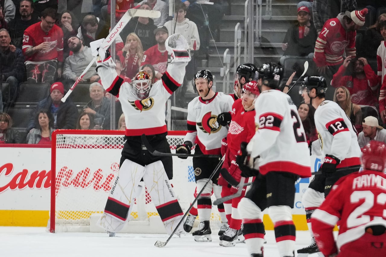 A hockey goaltender raises both arms in the air to celebrate a win.