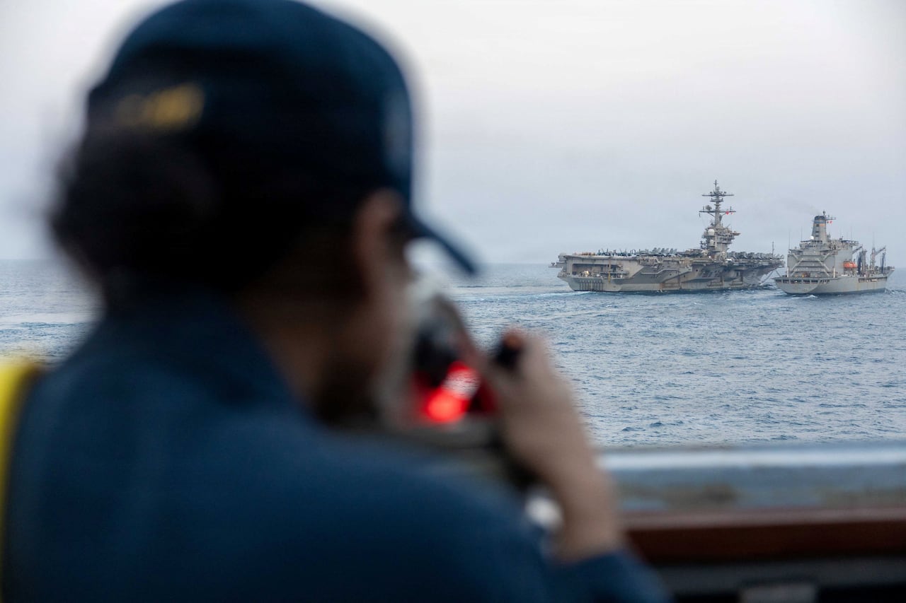 A person looks out at an aircraft carrier in a body of water.