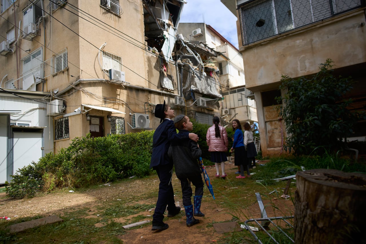 Several people, including youth, look up at damaged buildings. 