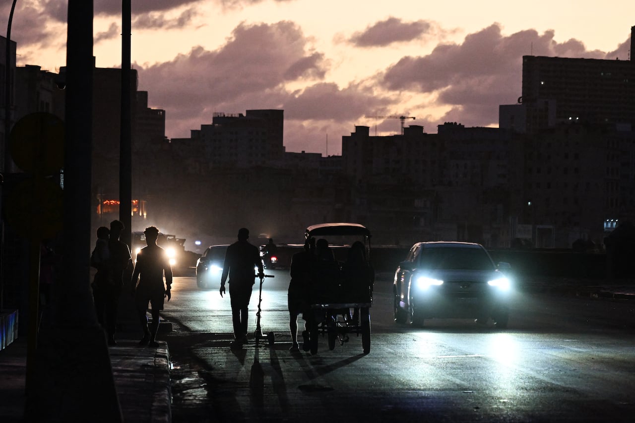 two people walk on the street at night beside a car with headlights on 