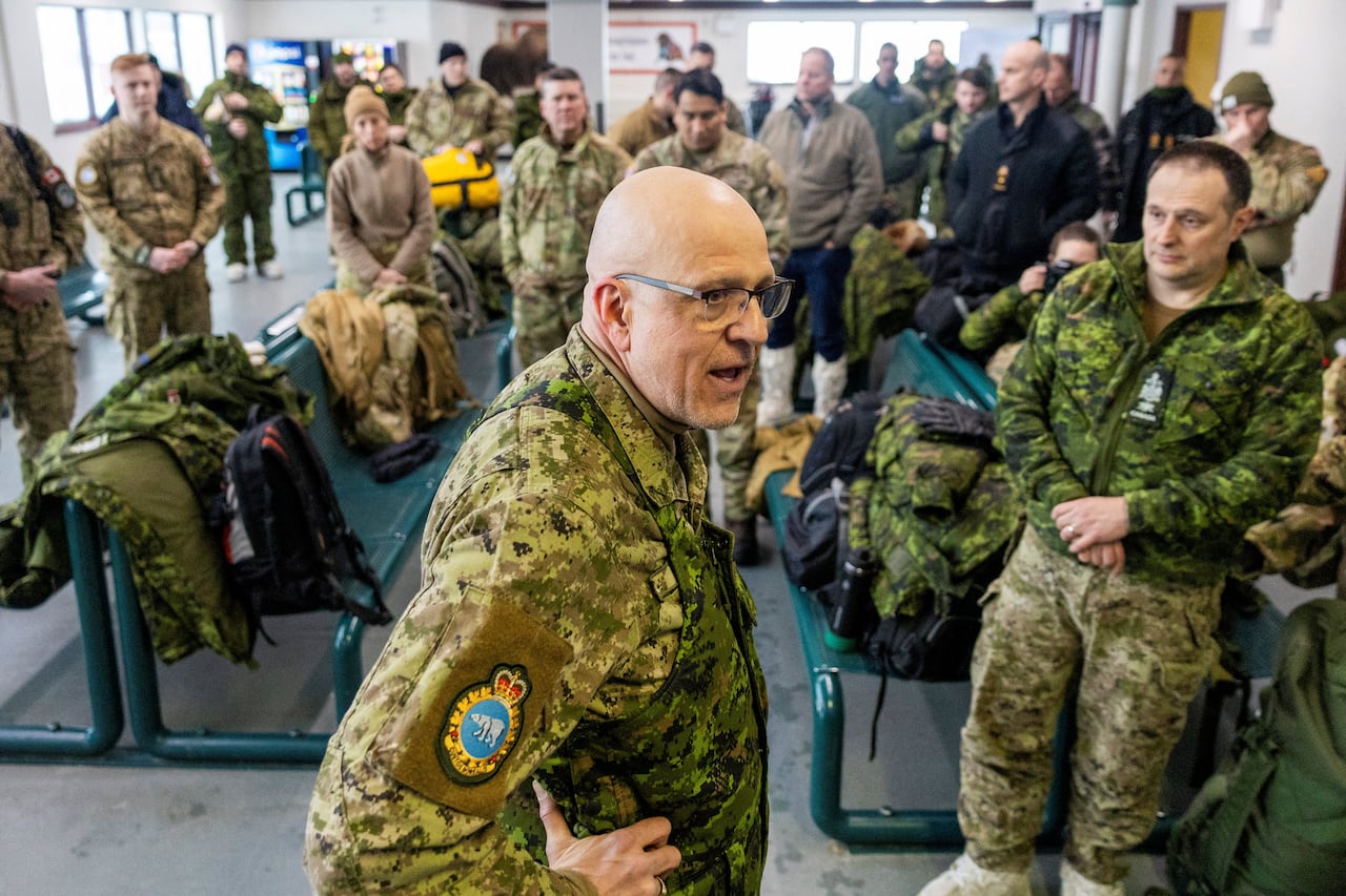People, most of whom are wearing military fatigues, stand in a room. 