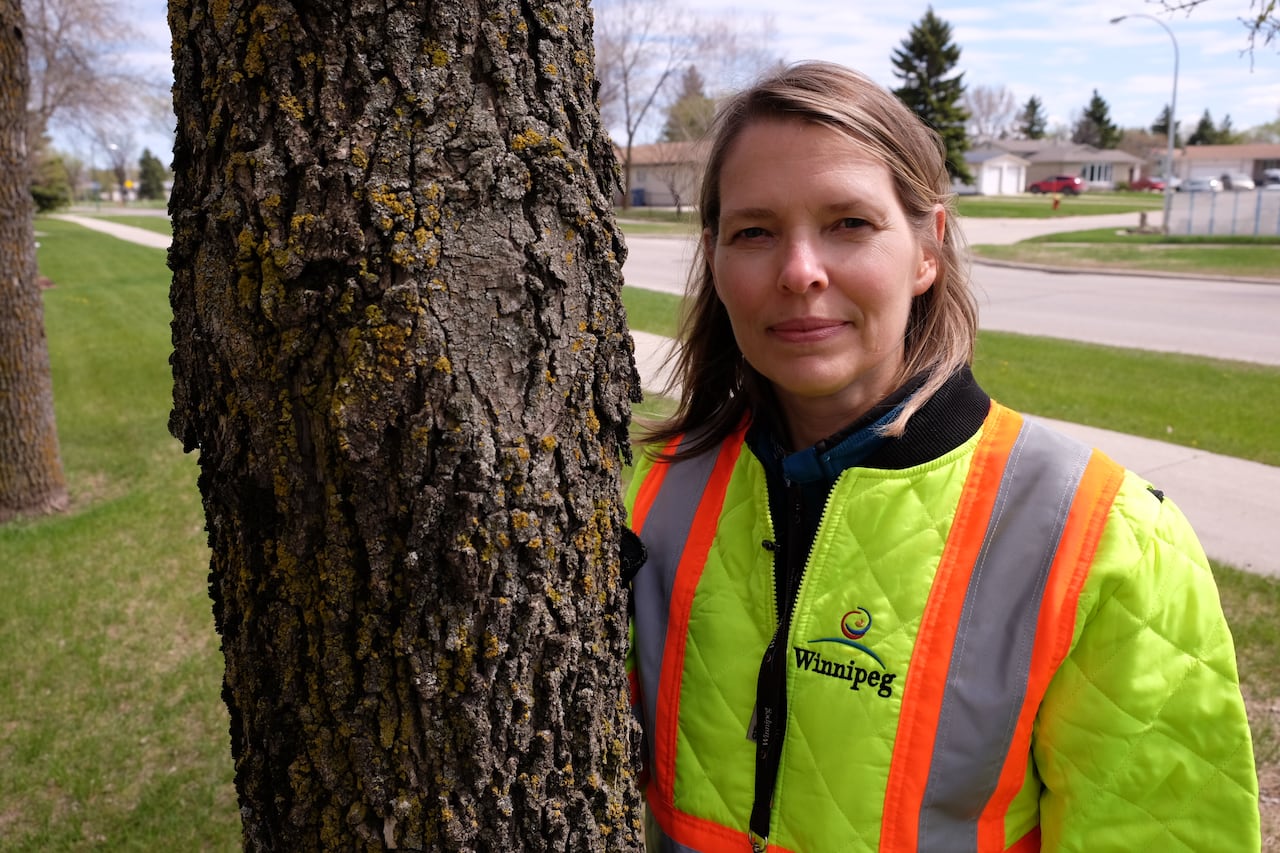 A woman with a green jacket stands besides a tree.