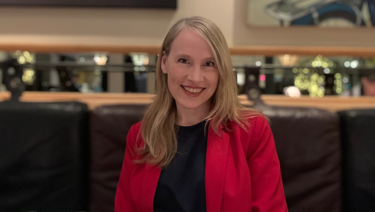 A smiling woman wearing a black top and red jacket. 