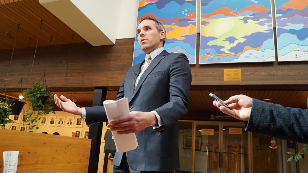 A man in a suit speaks in a media scrum.