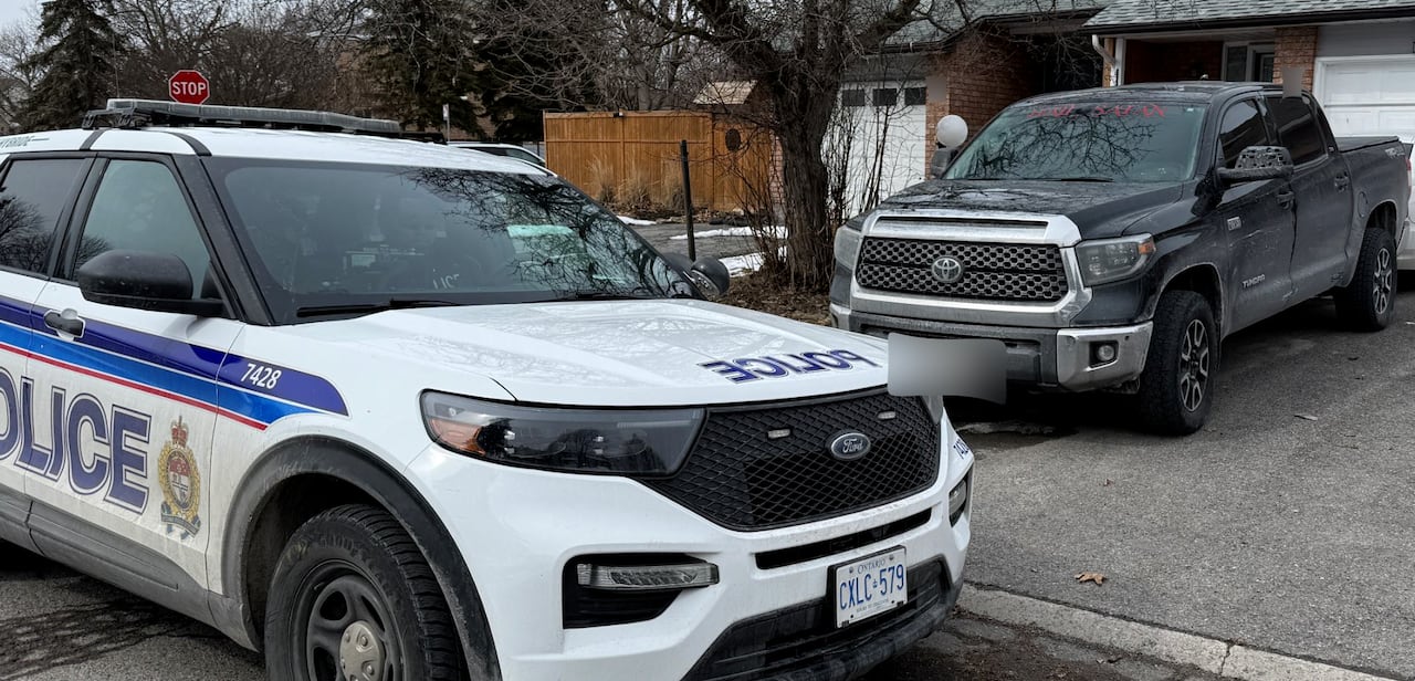 An image of a truck being blacked in its driveway by a police car