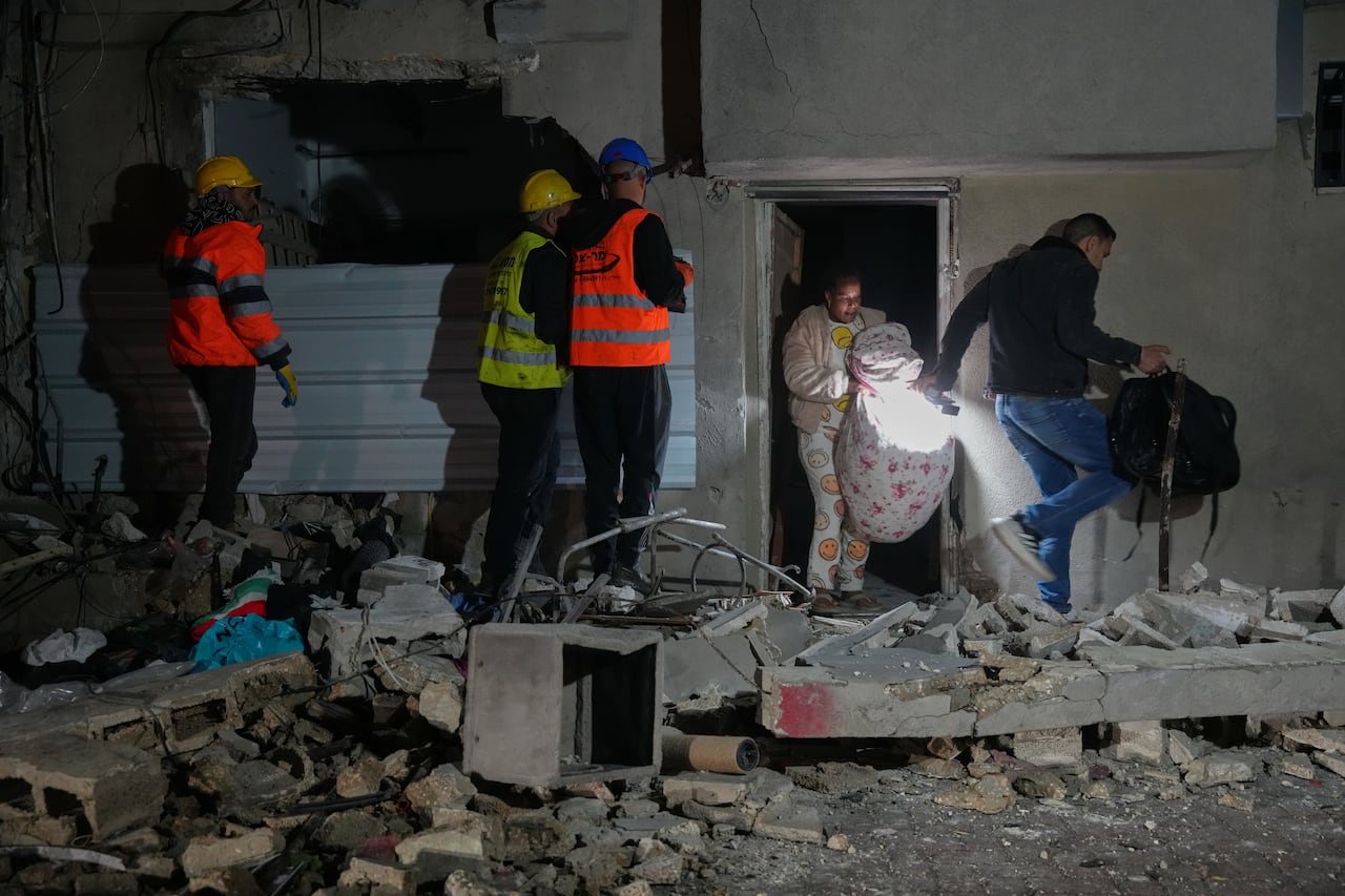 Residents carry personal belongings as they leave a building damaged in a missile strike.