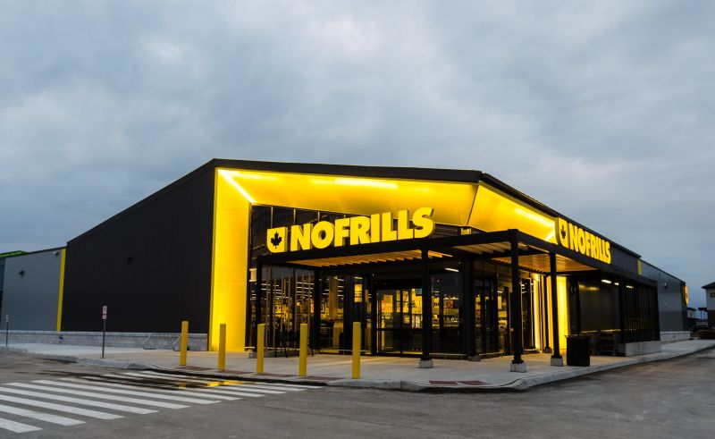 Modern Nofrills grocery store with bright yellow signage and black facade, located in Toronto, Ontario, under a cloudy sky, featuring large glass windows and a welcoming entrance.