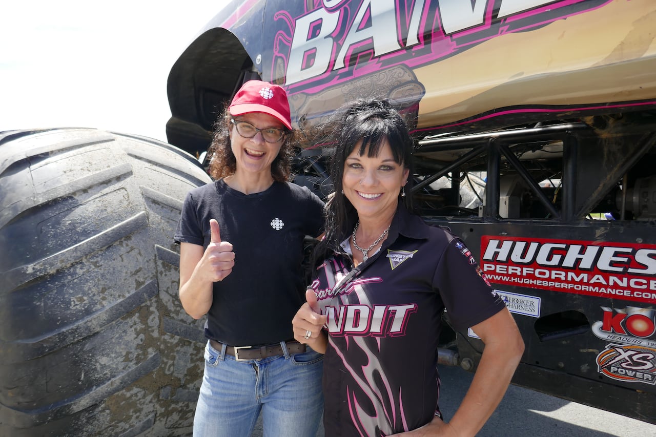 Two women standing in front of a monster truck, both giving a thumbs up.