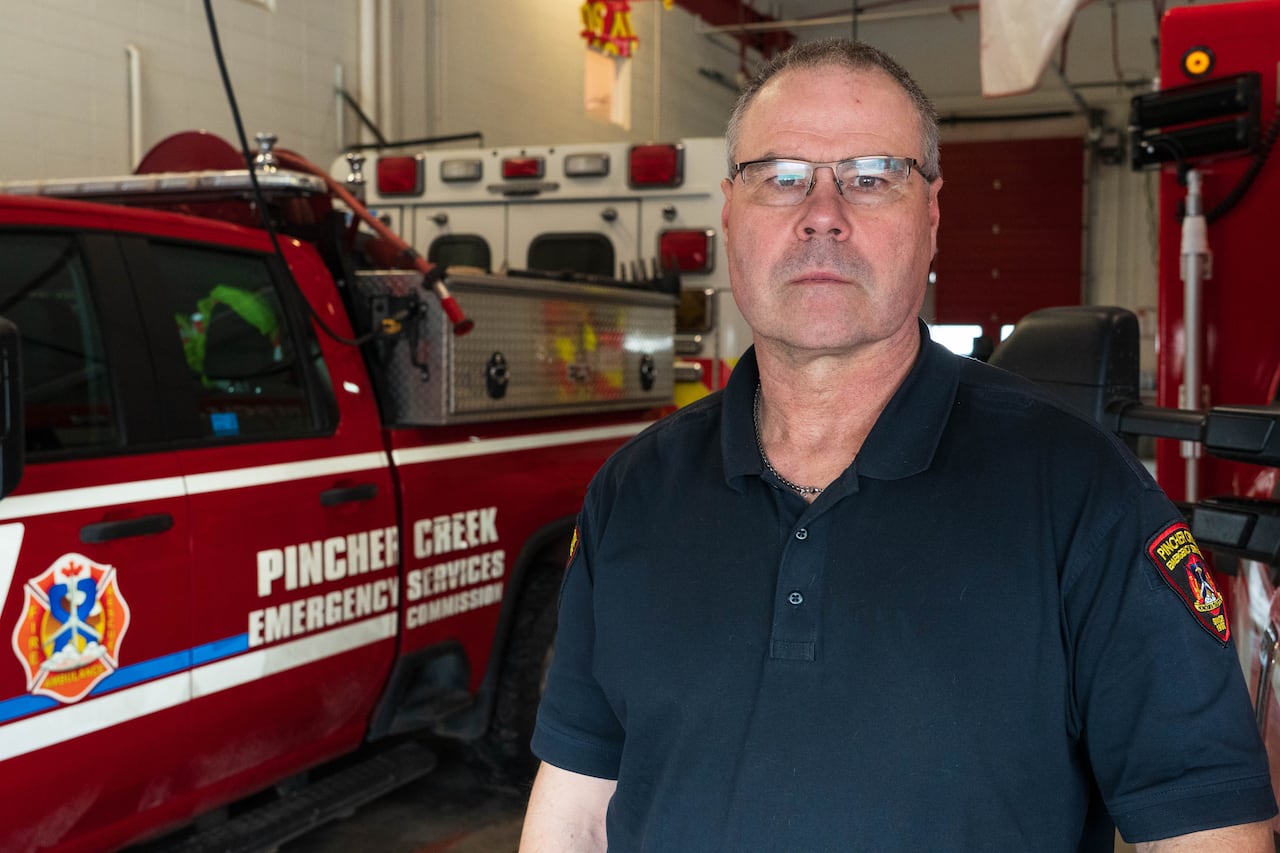 Medium shot of a man in a dark blue shirt in front of a red emergency vehicle 