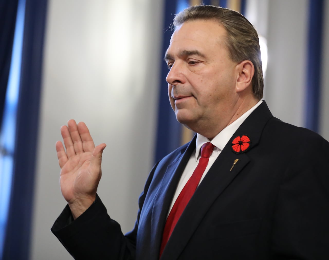 A man raises his right hand. He is wearing a blue suit with a red tie.