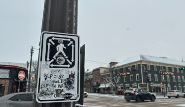 A graffiti-covered sign demonstrates how to use a scramble crosswalk at Whyte Avenue and Gateway Boulevard.