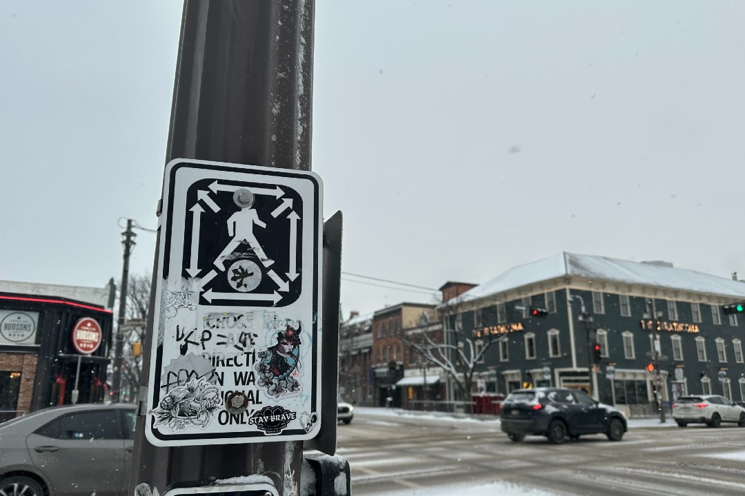 A graffiti-covered sign demonstrates how to use a scramble crosswalk at Whyte Avenue and Gateway Boulevard.