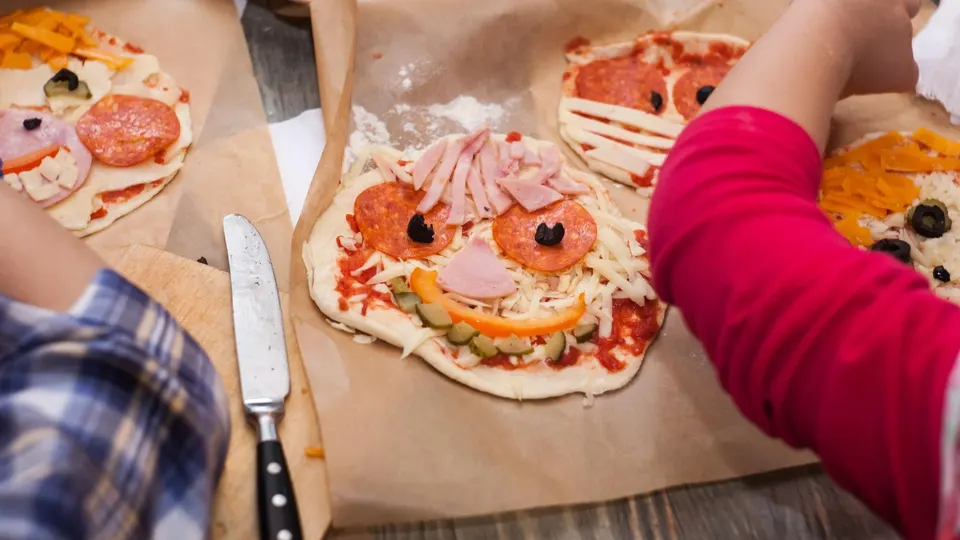 Master class for children on baking funny halloween pizza. Young children learn to cook a funny monster pizza. Kids preparing homemade piizza. Little cook.