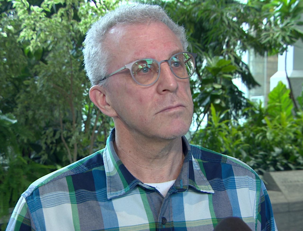 Colin Laroque is inside a university campus building with green plants behind him