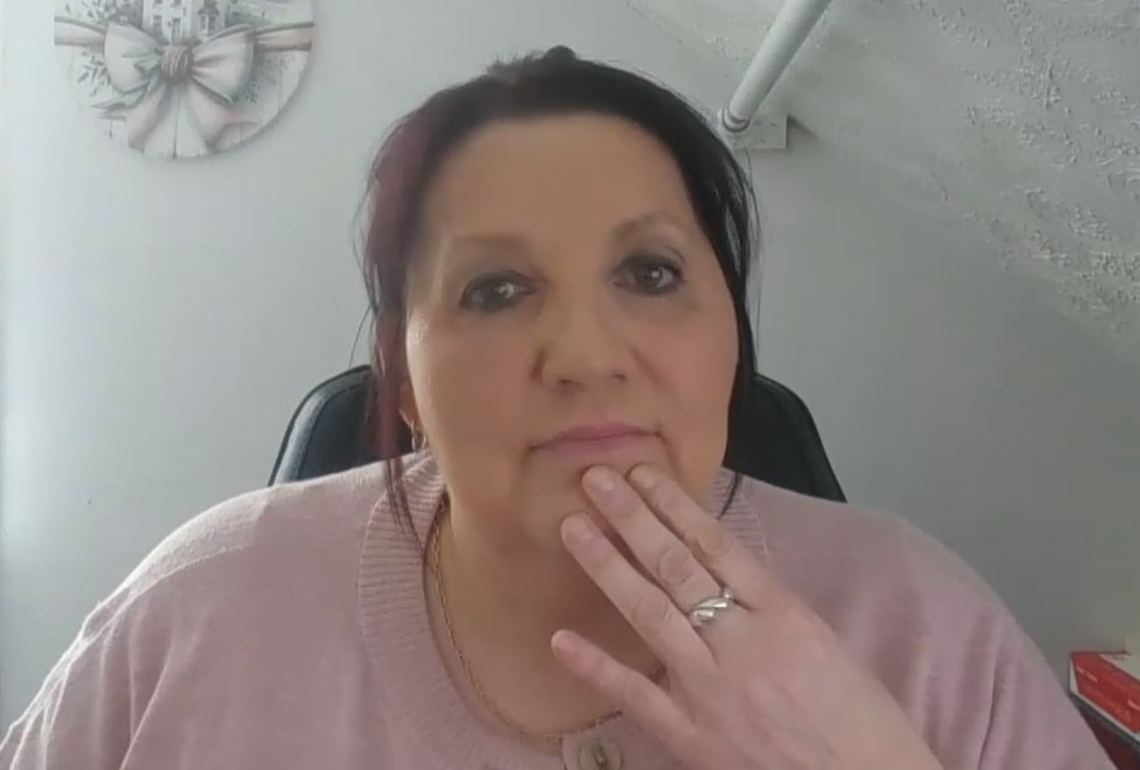 Yvette Jarvis sits wearing a pink top looks into the camera with a hand on her chin. 
