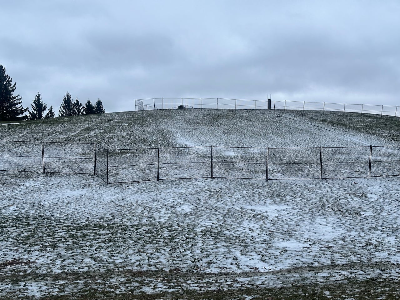 A fenced-off hill with light snow on it.