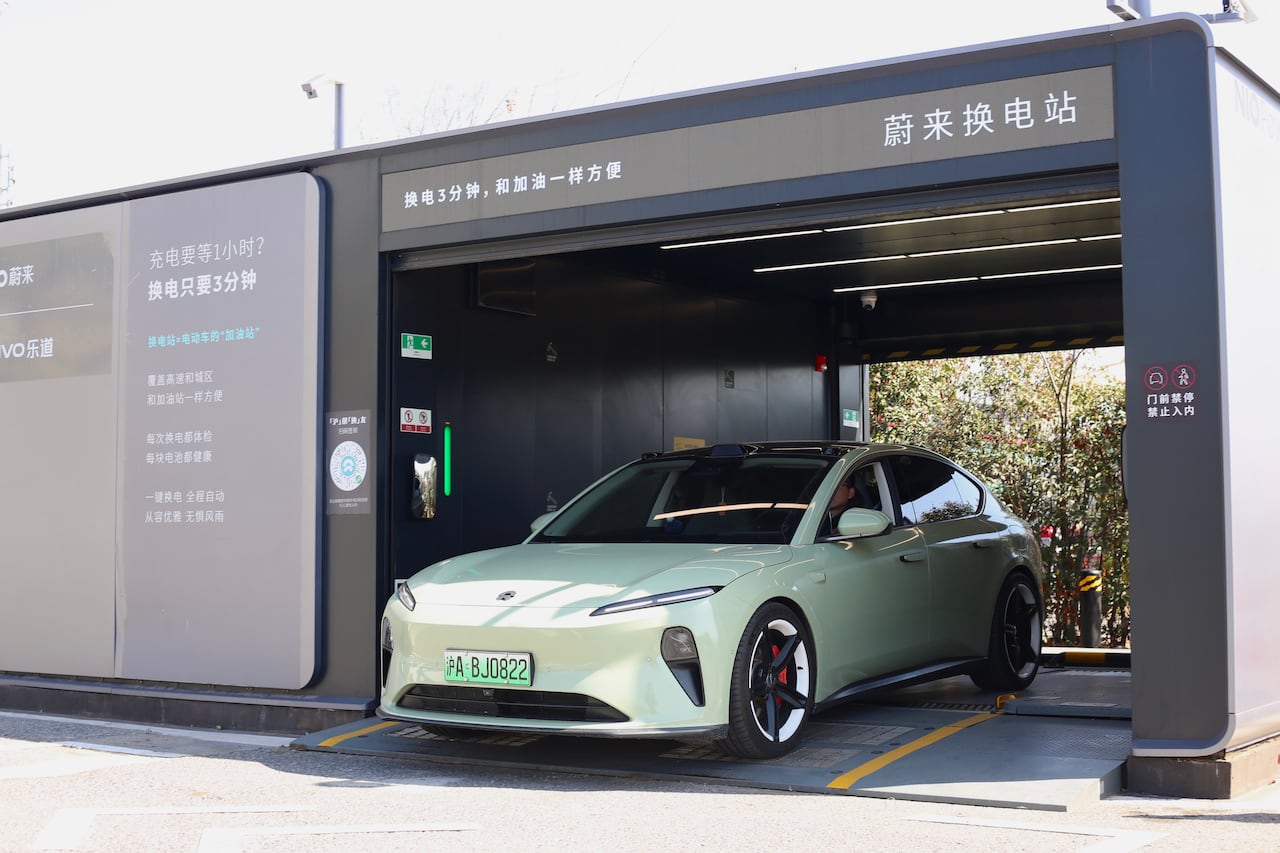 A pale green car sits inside a grey, garage-like structure.
