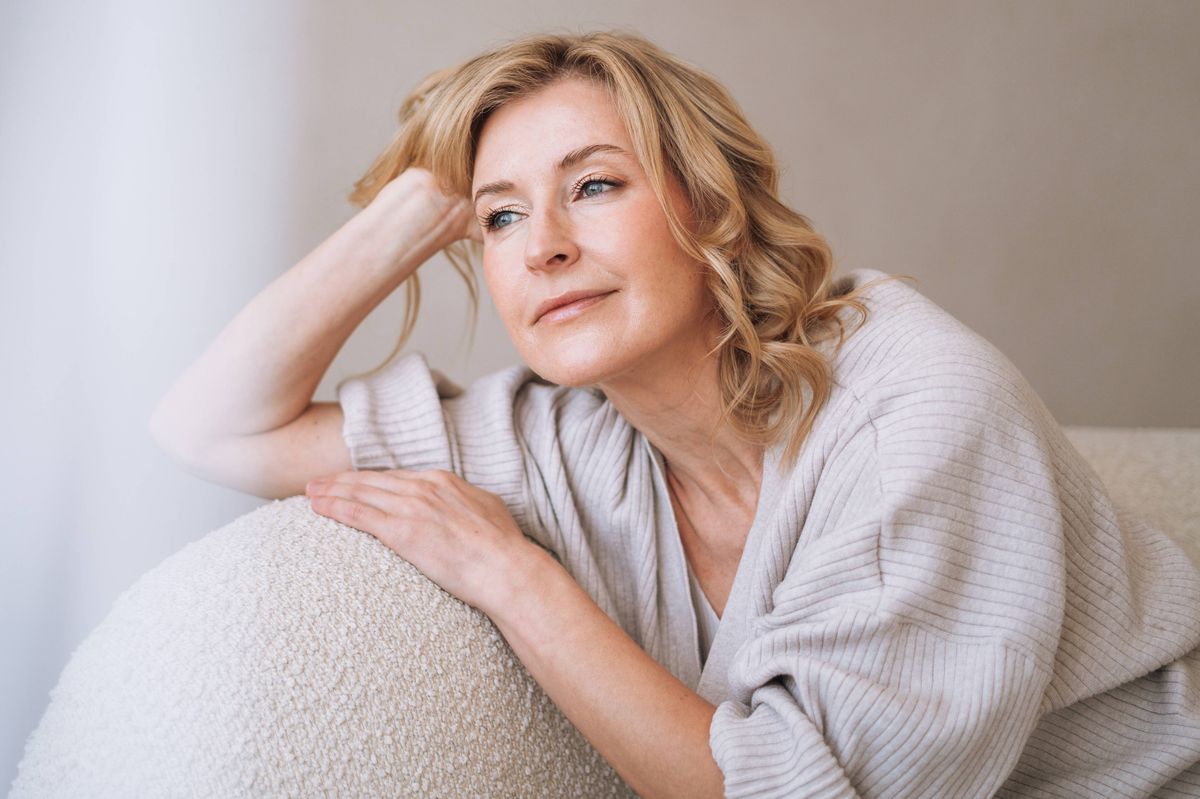 blonde woman in a warm knitted cardigan relaxing on a comfortable couch at home. Cozy interior, casual outfit, calmness, home leisure and winter comfort atmosphere